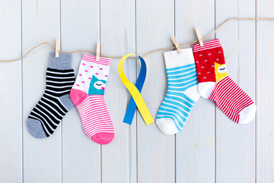 Children's socks with stripes and colors in clothesline on wooden background. In the center there is a yellow and blue ribbon. World Down Syndrome Day concept.