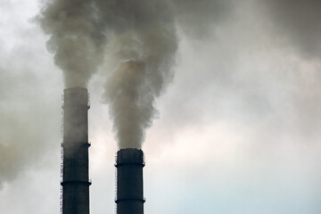 Coal power plant high pipes with black smoke moving up polluting atmosphere.