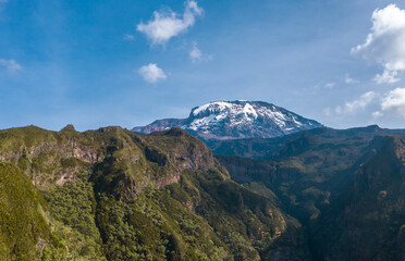 Aerial shot of a highest African continent summit - Kilimanjaro Uhuru Peak 5895m volcano covered with snows. Drone point of view flying up at cca 3600m. Umbwe route, Tanzanian National Park