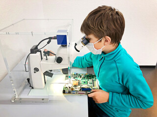 Kid boy conducts experiment with microscope in school lab. Curious inquisitive child learning...