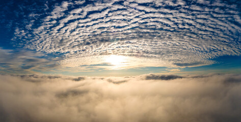 Aerial view of bright yellow sunset over white dense clouds with blue sky overhead.