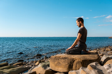 Attractive young man practicing yoga meditation and breathwork outdoors by the sea