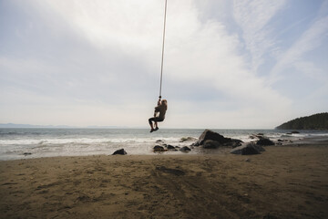 A young blonde woman swings on a rope swing at the scenic Mystic Beach located along the shores of...
