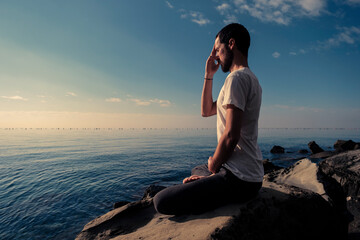 Attractive young man practicing yoga meditation and breathwork outdoors by the sea - obrazy, fototapety, plakaty