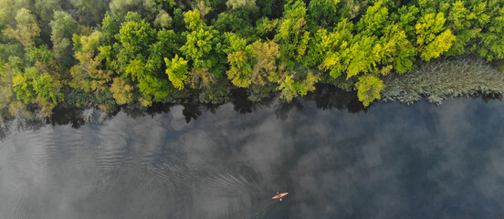 Top aerial view of the river along which a small orange kayak floats. Green trees grow on the shore. Banner. Ukraine, Europe