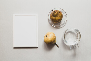 Modern still life with white empty photo frame. Summer composition with pears and a glass of water. Mock up flat lay on light background