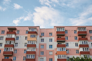 View from underneath on colorful pink apartment building in front of blue sky with clouds. City dwelling. Urban architecture concept.