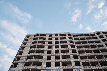 Fototapeta premium View from underneath on construction of grey concrete apartment building in front of blue sky with clouds. City dwelling. Urban architecture concept.