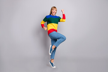 Full length body size photo of female student in striped colorful sweater gesturing like winner isolated on pastel grey color background