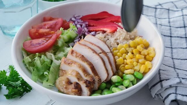 Grilled chicken breast with brown rice and vegetables in white plate, gray background. Healthy food concept.