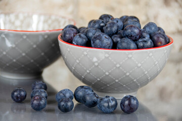 Blueberries in a bowl with a handful of loose ones in front and another empty bowl in the background
