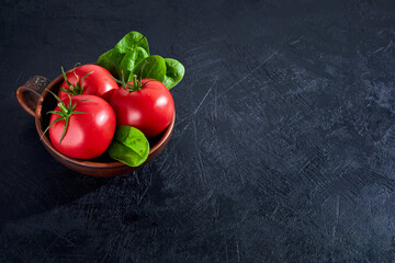 Fresh grape tomatoes with spinach Leaves on black stone background. Vegan veggies diet food. Herb,...