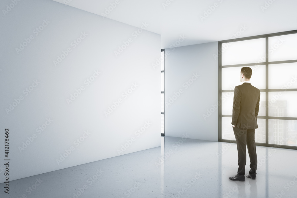 Poster back view on businessman staying on glossy floor in empty light room with city view and blank white 