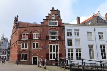 Fototapeta na wymiar Street View in Amsterdam with Historic Brick Building with Red Shutters and Stepped Gable