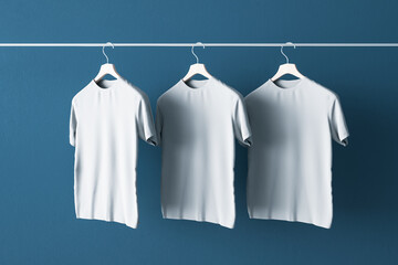 Put your sign concept with three blank white t-shirts hanging on blue concrete wall. Mockup. 3D...
