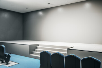 Modern performance hall with blank grey wall and podium, one row of seats on blue carpet and round lights on ceiling. 3D rendering