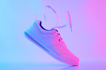 Hand hold white sneakers with flying laces in neon light. Sport shoes for training in the gym....