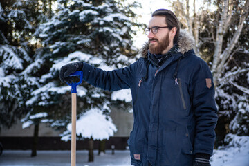 Man in winter clothes holding a handle of a snow shovel. Shoveling snow, winter household chores.