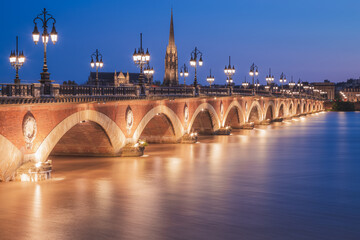 Obraz premium The historic Pont de Perre illuminated at night over the River Gardonne in Bordeaux, France with Bordeaux Cathedral in the background.