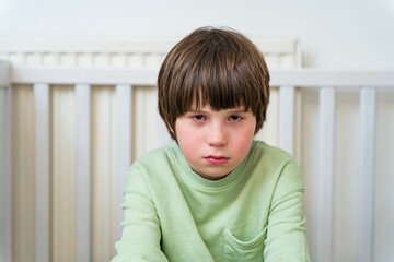 Portrait of an unhappy and sad boy of ten years old sitting alone at home. Depressed child showing emotions.