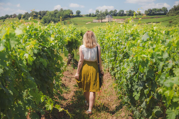 A young blonde caucasian female tourist explores vineyards at Saint-Emilion in the Bordeaux wine country region of France on a sunny summer holiday.