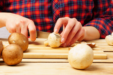Close-up of female hands are cutting mushrooms on a cutting board.