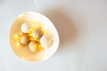 Stylish Easter festive eggs in natural color on a Black background with garlands with feathers in wihte bowl on pink linen.