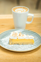 White cup of coffee with piece of cake in saucer on the wooden table