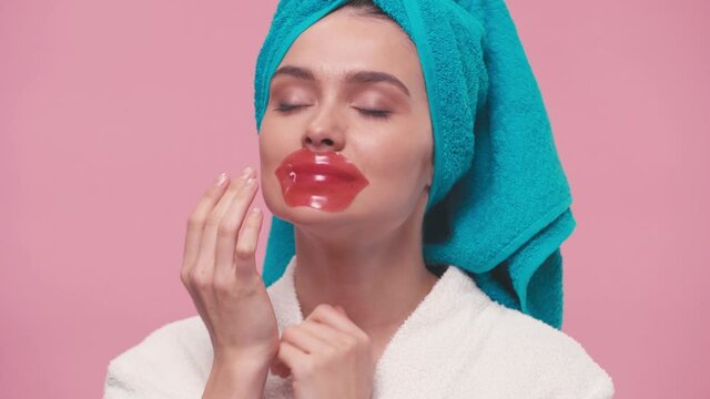 young woman with towel on head applying lip mask isolated on pink