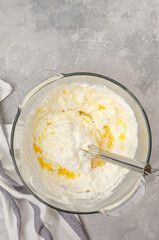 Whipped egg whites with flour and butter in a bowl on a gray concrete background. Cooking a vanilla cake with blueberries. Recipe step by step. Top view.