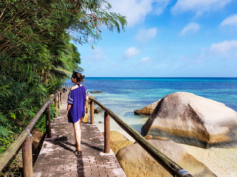 Woman In Beach Coverup Walking On A Wooden Footpath Over A Sandy Golden Beach.