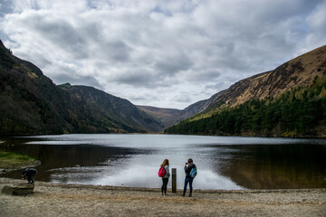 Fototapeta na wymiar Dos jóvenes observan un lago entre colinas y con nubes que amenazan lluvia.