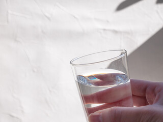 水が入った透明コップを持つ手。水分補給、水を飲む。