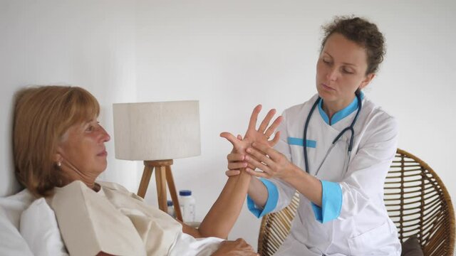 Health worker woman performing diagnosis test on the patients hand to check on arthritis.Treating older adults at their homes