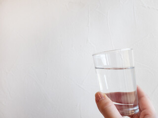 水が入った透明コップを持つ手。水分補給、水を飲む。