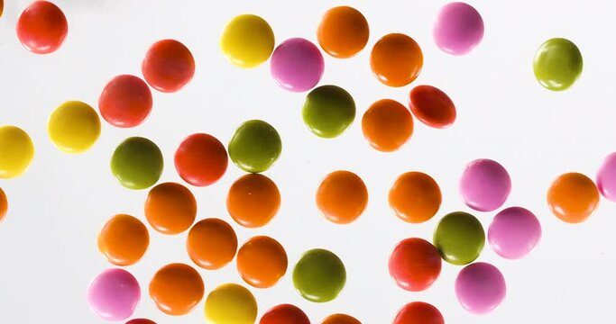 A hand sweeps a bunch of colorful dragee chocolate off the glass background. Woman hand. Slow motion. Close up.