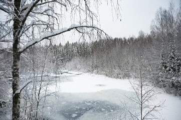 Winter nature landscape with a frozen river in the snow covered forest