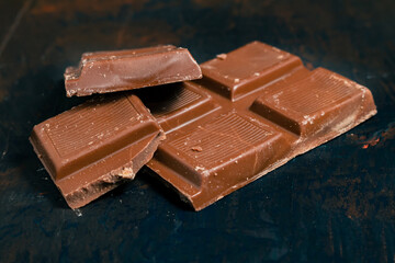 Tablet pieces of dark chocolate on a dark surface.