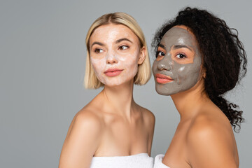 Young multicultural women with facial masks standing isolated on grey