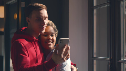 Multiethnic couple checking smartphone standing next to window at home