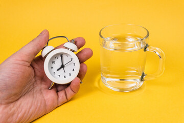 Alarm clock and a glass of water on a yellow background. Wake up early in the morning. Drink water