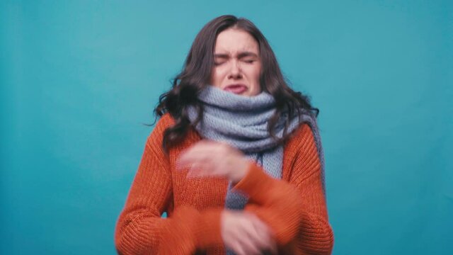 sick woman in scarf freezing and sneezing isolated on blue