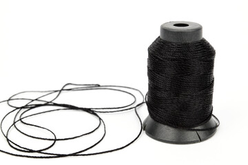 Spool of black nylon thread. A small part of the thread from the spool lies unrolled nearby.