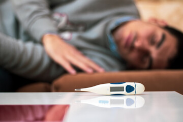 thermometer leaning on a table in a living room while a person is sleeping behind