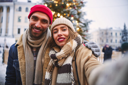 Jolly young couple taking selfie at Christmas Tree outdoors