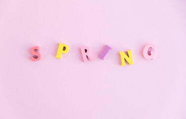The word SPRING in wooden color letters on a pink pastel background