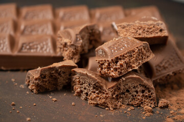 Different pieces of dark chocolate and cocoa powder on a dark surface.