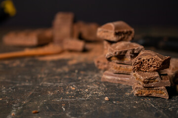 Different pieces of dark chocolate and cocoa powder on a dark surface. Space for text