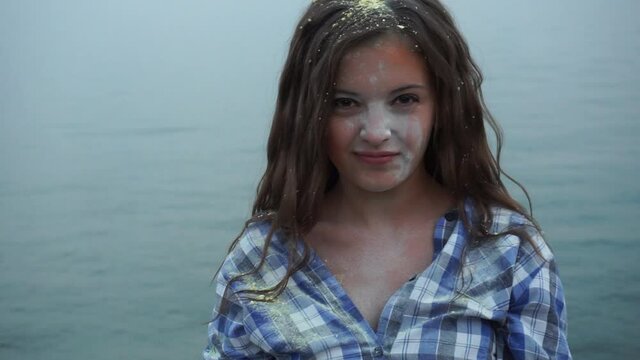 Portrait of a beautiful girl at the sea in holi paints, throws colored dust and has fun smiling