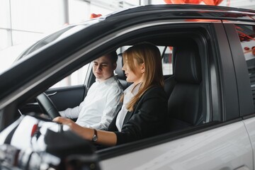 Visiting car dealership. Beautiful couple is looking at camera and smiling while sitting in their new car